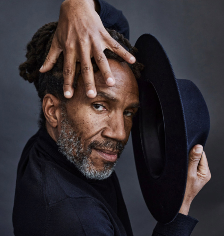 Clarence Brooks posing with a hat in one hand and the other hand spread over the top of his face.
