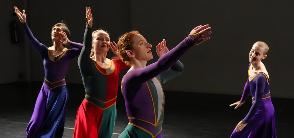 Four dancers wearing long dresses, running, with joyful expressions.